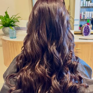 Glossy, chocolate-brown hair with subtle, warm-toned highlights styled into soft, flowing waves fabu